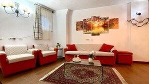A living room with two sofas, a coffee table, a chandelier, and a wall with a sunset painting. - 3 bedroom awesome apartment in Peglio (Peglio)
