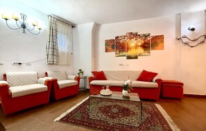 Ein Wohnzimmer mit zwei Sofas, einem Couchtisch, einer Chandelierleuchtre und einer Wand mit einem Sonnenuntergangsgemälde.