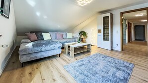 A modern loft bedroom with a sloped ceiling, a large gray sofa, a wooden coffee table, and a blue rug. - Alexanders Domizil by Interhome (Schonach)