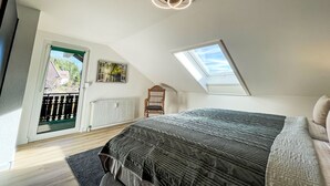 A bedroom with a skylight, a bed with a dark quilt, a radiator, and a window with a view of greenery. - Alexanders Domizil by Interhome (Schonach)