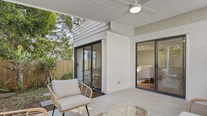 Eine Terrasse mit Korbmöbeln, einem Deckenventilator und einer Schiebetür zu einem Innenraum.