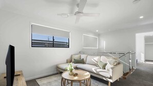Ein modernes Wohnzimmer mit einer Couch, einem Couchtisch, einem Fernseher und einem Deckenventilator.