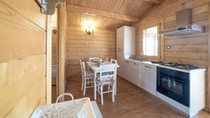 Interior de una cabaña de madera con comedor, cocina y ventana que proporciona luz natural.