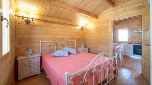 Un dormitorio de cabaña de madera con cama, mesitas de noche y una pequeña zona de escritorio.