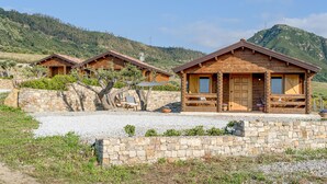 Una cabaña de madera rústica con un muro de piedra frontal, ubicada en una zona montañosa.