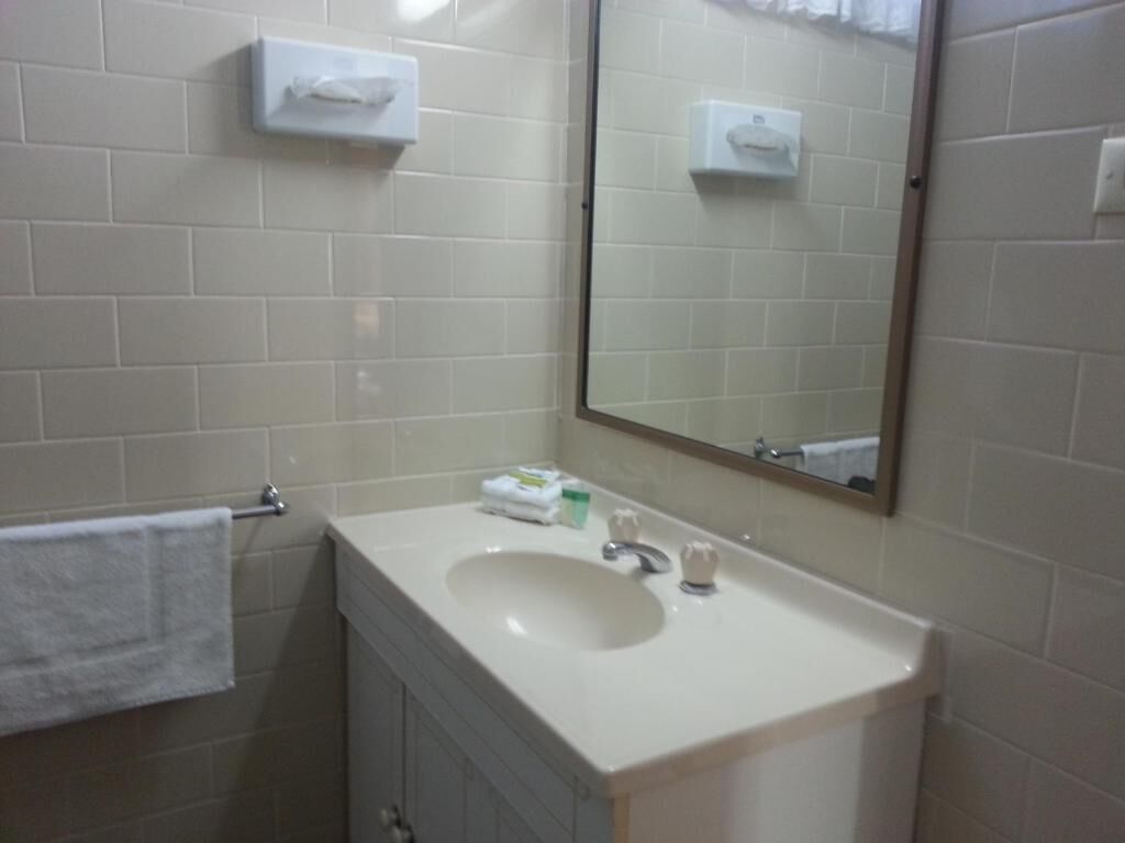 Un baño con un lavamanos blanco, un espejo y un perchero para toallas.