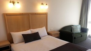 Une chambre d’hôtel avec un grand lit, deux tables de chevet, un fauteuil vert et une fenêtre avec des rideaux.