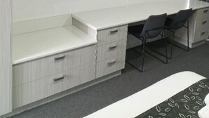 Une chambre moderne dotée d’un téléviseur à écran plat fixé au mur, d’un bureau blanc avec des tiroirs, de deux chaises et d’un lit recouvert d’une couvre-lit à motifs.
