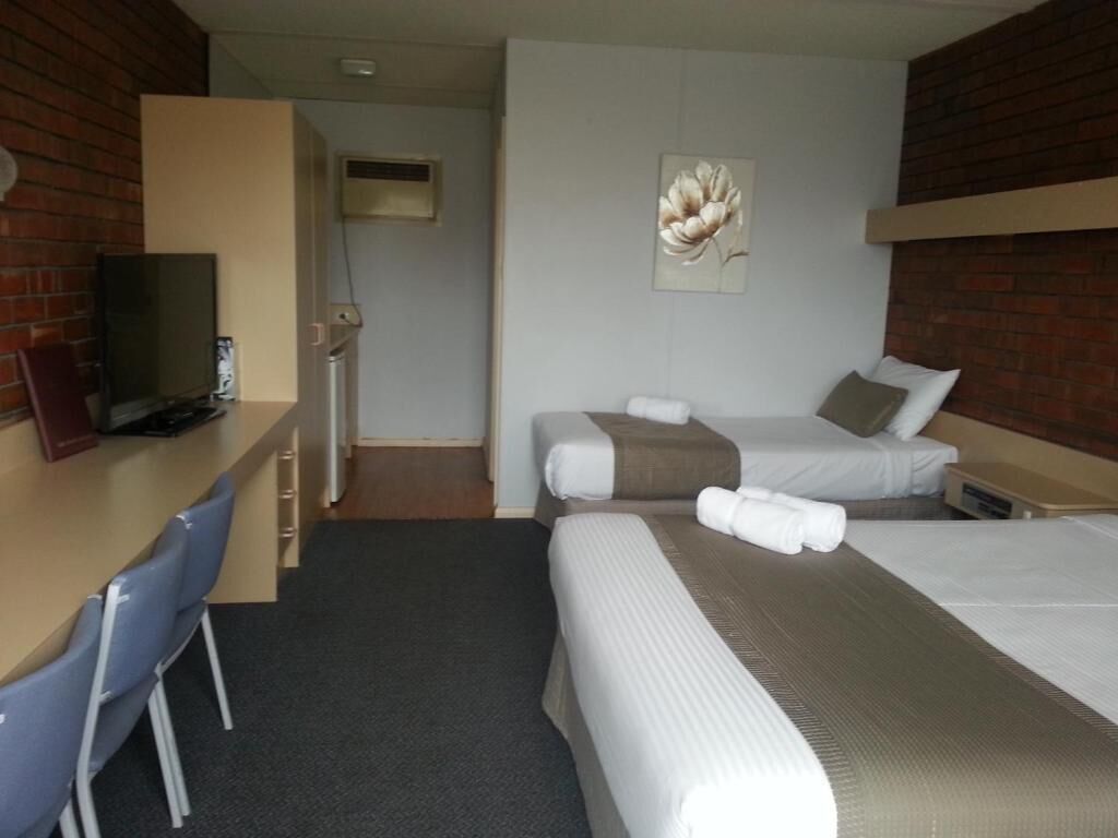 Una habitación de hotel con dos camas, un escritorio con silla, un televisor y un cuadro en la pared.