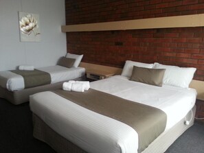 A hotel room with two beds, each with white bedding and brown headboards. There is a brick wall behind the beds and a painting of a flower on the wall to the left. - Big Valley Lakeside Paradise Motor Inn (Shepparton)