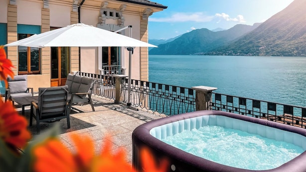 Eine Terrasse mit Sitzgelegenheiten im Freien, einem Whirlpool und Blick auf einen See und Berge.