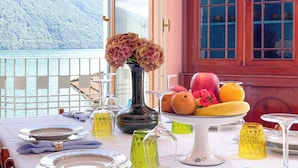 Ein Tisch gedeckt mit Tellern, Gläsern und einer Obstschale, mit Blick auf einen malerischen See und Berge.