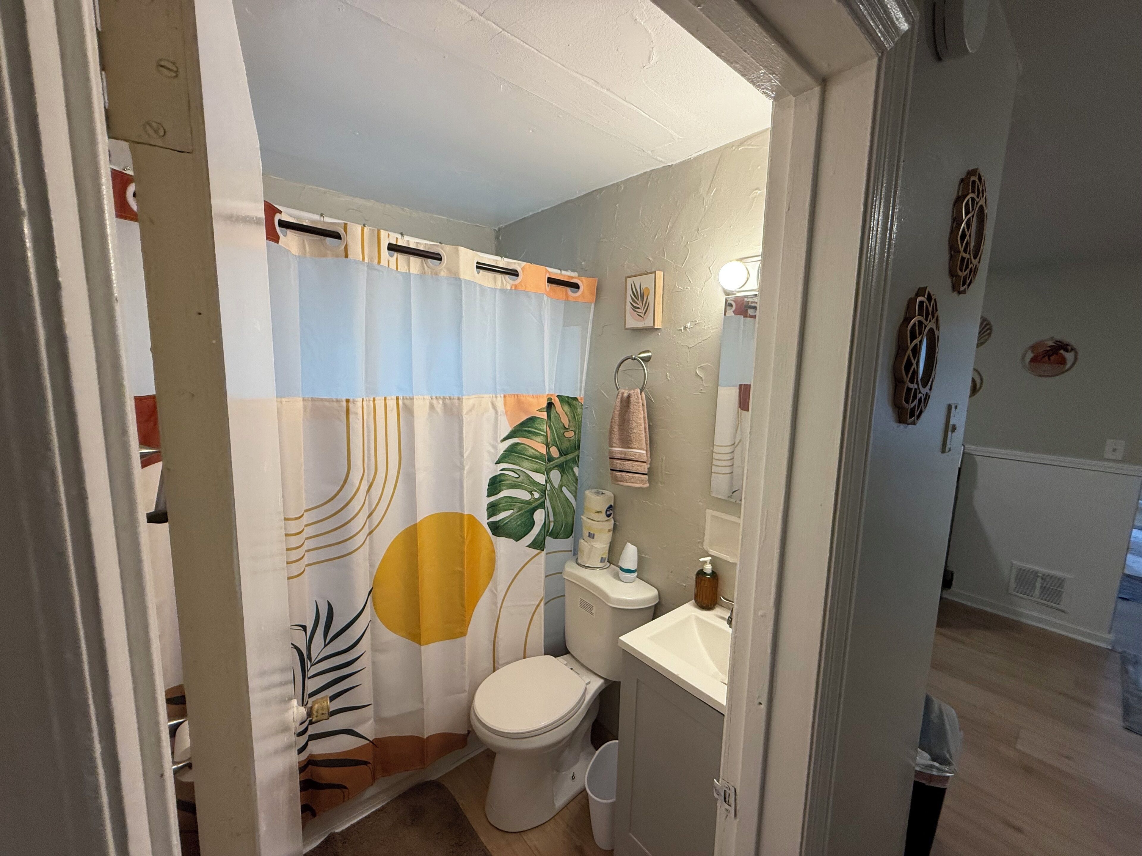 Un baño con inodoro, lavamanos y cortina de ducha con estampado de hojas tropicales.