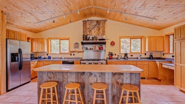 Una cocina amplia con armarios de madera, una isla central con taburetes, un refrigerador de acero inoxidable y un ventanal grande.