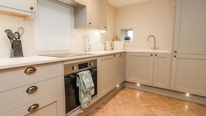A modern kitchen with light-colored cabinets, a stainless steel oven, and a herringbone-patterned wooden floor. - Henside Cottage (Settle)