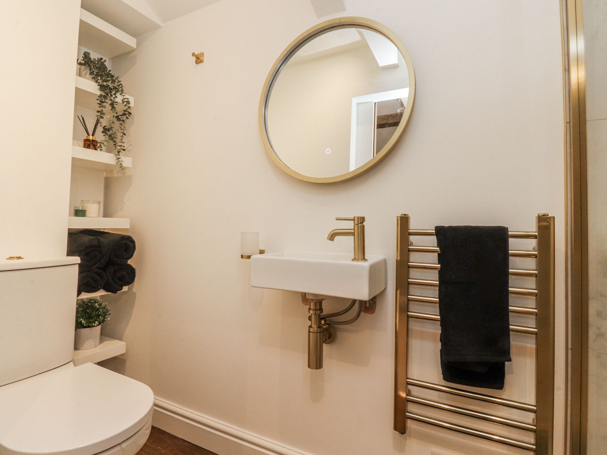 A bathroom with a white toilet, a gold sink, a round mirror, and a towel rack.
