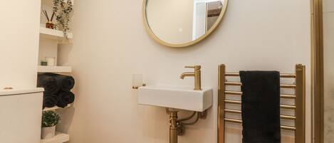 A bathroom with a white toilet, a gold sink, a round mirror, and a towel rack.