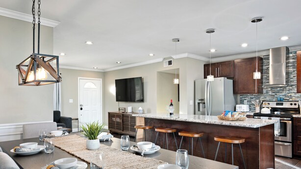 Una cocina moderna con una isla central, taburetes de bar y un comedor con una mesa dispuesta para cuatro.