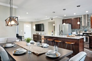 A modern kitchen with a central island, bar stools, and a dining area with a table set for four. - 5 Beds w/ Heated Pool By Old Town & ASU, Dogs Welcome! (Tempe)