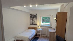 Un dormitorio pequeño y luminoso con una cama individual, un escritorio, una silla y una ventana con vistas a zonas verdes.
