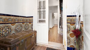 Une pièce avec un banc en bois, une porte blanche ornée d’un vitrail et un mur à motifs.