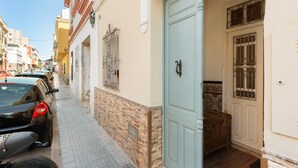 Une rue étroite, bordée de voitures garées, et un immeuble avec une porte bleu clair et des barreaux décoratifs aux fenêtres.