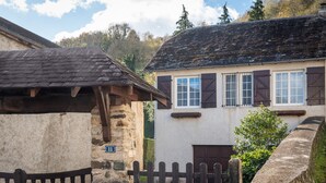 Un edificio de piedra rústico con una verja de madera, un muro de piedra con placa numérica y un pequeño jardín.