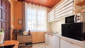 Una cocina compacta con armarios de madera, microondas, refrigerador y ventana con cortinas.