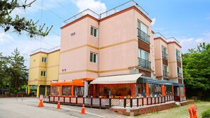 A multi-story hotel with a pink facade, outdoor seating area, and a visible balcony on the upper floors. - Ondam Pension (Incheon)