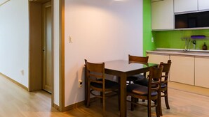 A dining area with a wooden table and chairs, a hanging light fixture, and a kitchen with green tiles and white cabinets. - Ondam Pension (Incheon)