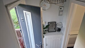 A hallway with a door leading to a garden, a wall-mounted clock, a welcome sign, and a small shelf with decorative items. - 3 bed House, Sleeps 5, Near Airport and Town, Outside Parking Free (Manchester)