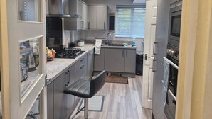 A modern kitchen with grey cabinets, a stainless steel range hood, a built-in oven, and a microwave. - 3 bed House, Sleeps 5, Near Airport and Town, Outside Parking Free (Manchester)