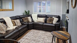 A modern living room with a dark leather sectional sofa, a patterned rug, and a wooden side table. - 3 bed House, Sleeps 5, Near Airport and Town, Outside Parking Free (Manchester)