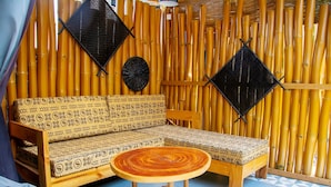 A room with a patterned sofa, a round wooden table, and a bamboo wall. - Hôtel Ô Balkan (Lomé)