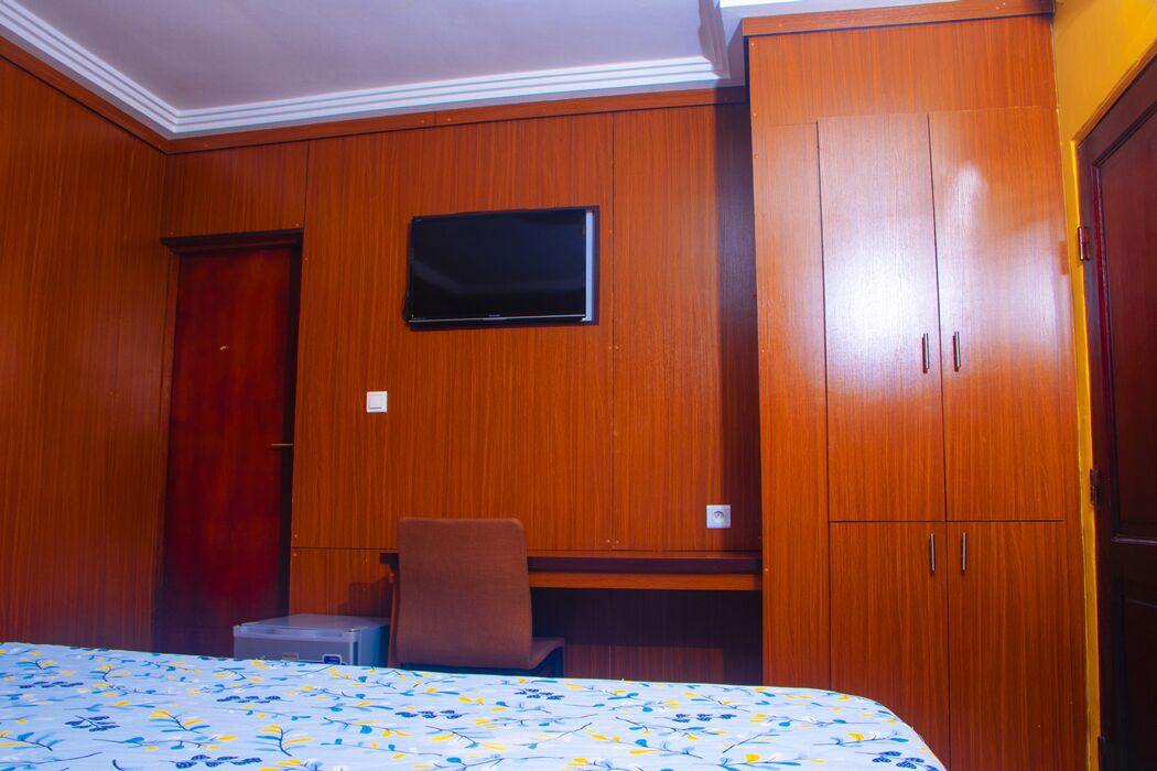 Ein Hotelzimmer mit Holzwandverkleidung, einem Bett mit Blumendekor, einem Schreibtisch mit Stuhl und einem an der Wand befestigten Fernseher.
