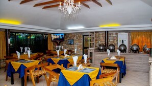 A restaurant with tables set for dining, a chandelier, and a stone wall with a fireplace. - Hôtel Ô Balkan (Lomé)