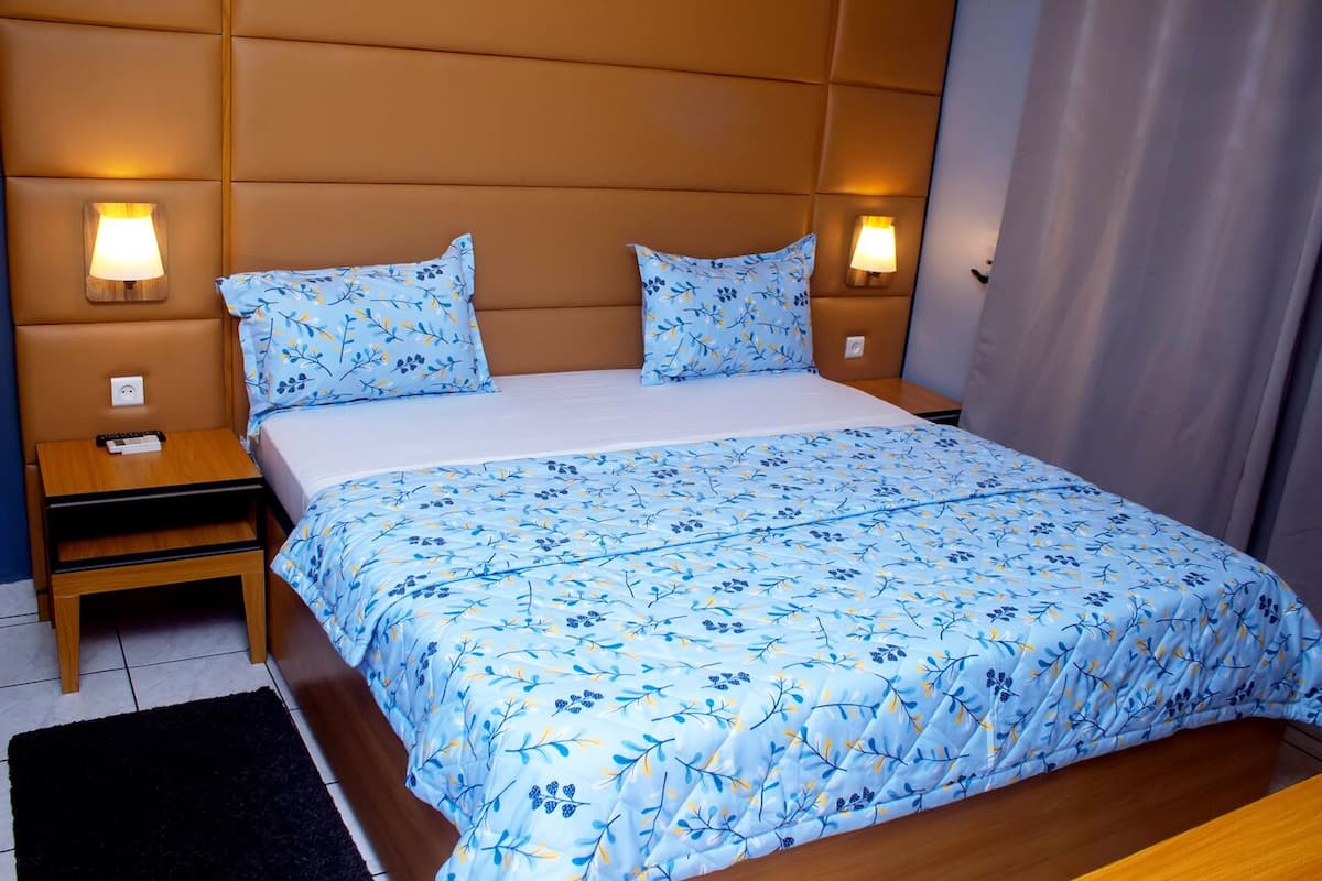 A neatly made bed with a floral bedspread, two bedside lamps, and a dark rug.