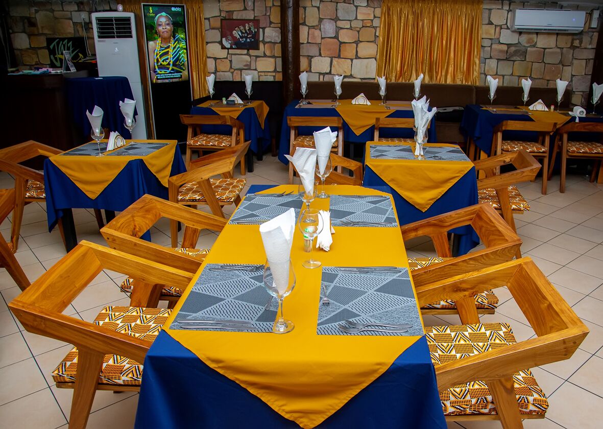 A restaurant with multiple tables set with yellow and blue tablecloths, wooden chairs, and white napkins.
