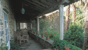 A covered outdoor area with stone walls, potted plants, and a seating area with wicker chairs. - Pazo de Andeade (Touro)