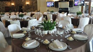 A banquet hall with round tables set for dining, white chairs, and potted plants. - Pazo de Andeade (Touro)