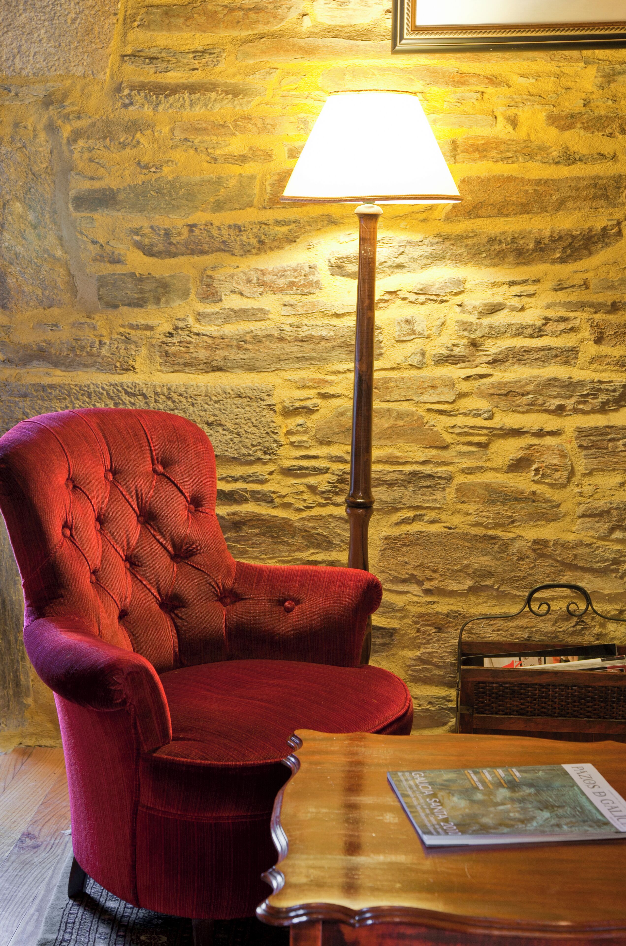 A red upholstered armchair next to a wooden table with a lamp and a book.