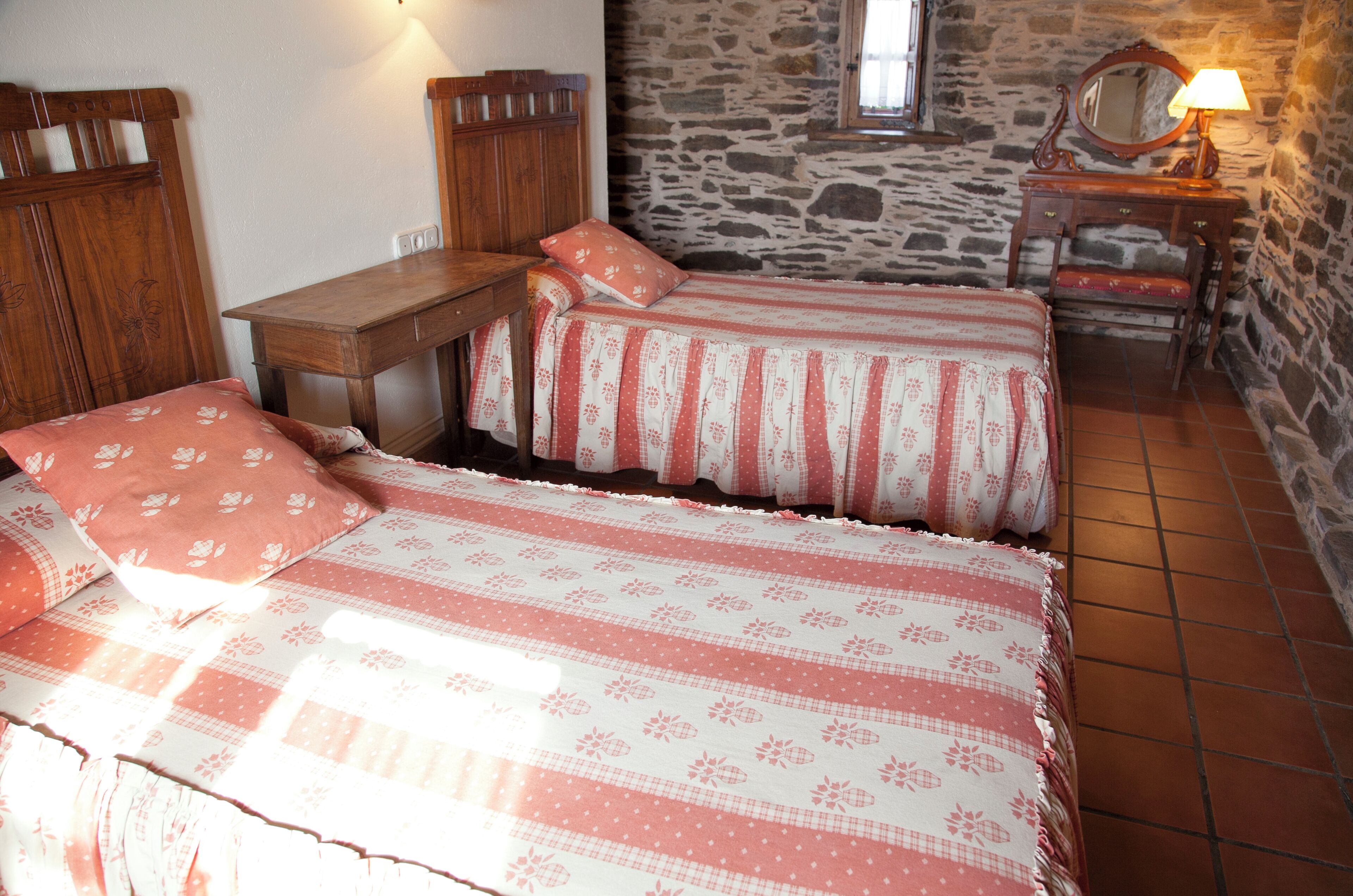 Un dormitorio con dos camas, un aparador de madera, una pared de piedra y una ventana.