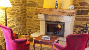 A cozy room with a stone wall, a fireplace, two red armchairs, a wooden table, and a floor lamp. - Pazo de Andeade (Touro)
