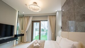 Habitación de hotel moderna con una cama grande, un televisor de pantalla plana, una puerta de vidrio que da a un balcón y una pared de acento de piedra.