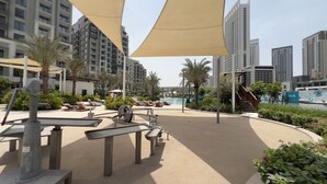Zona de piscina de un resort con tumbonas, un tobogán acuático y vistas a edificios altos.