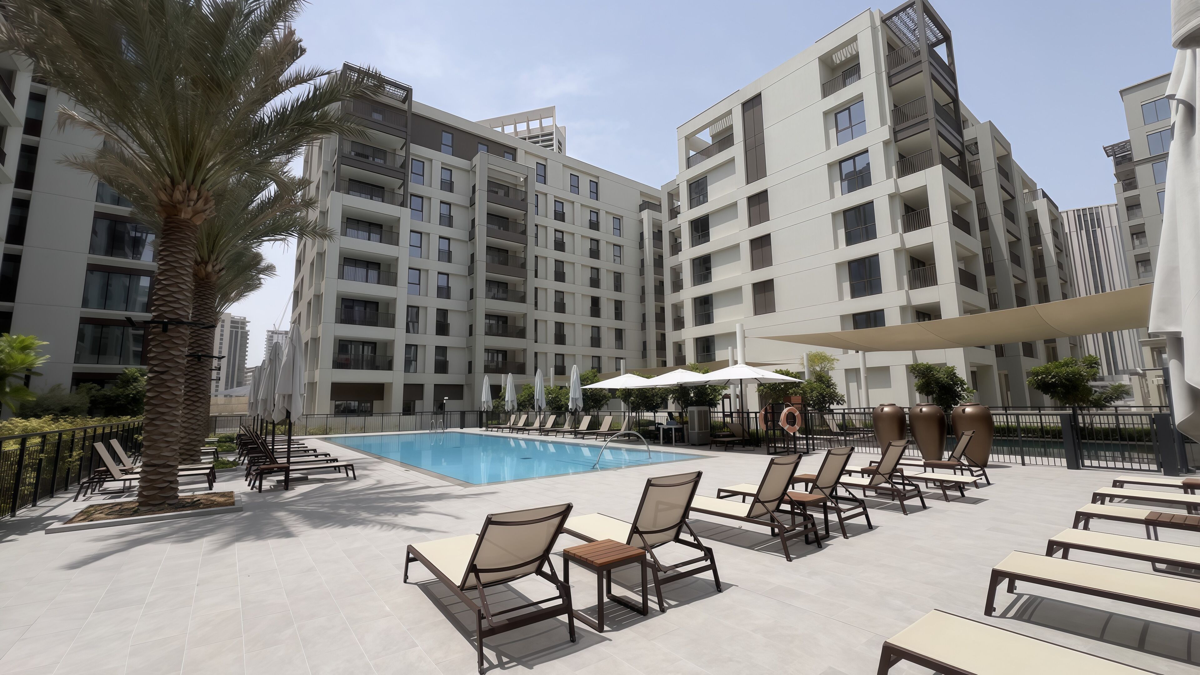 A modern hotel with a swimming pool, sun loungers, and a palm tree.