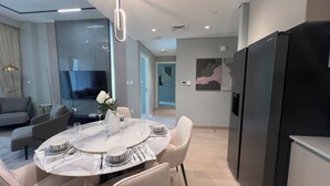 Una sala de estar moderna con comedor, televisor de pantalla plana y un refrigerador grande.