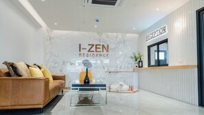 A modern reception area with a marble wall, a reception desk, a sofa, and a small table with a vase. - I-Zen Residence Central Eastville (Bangkok)