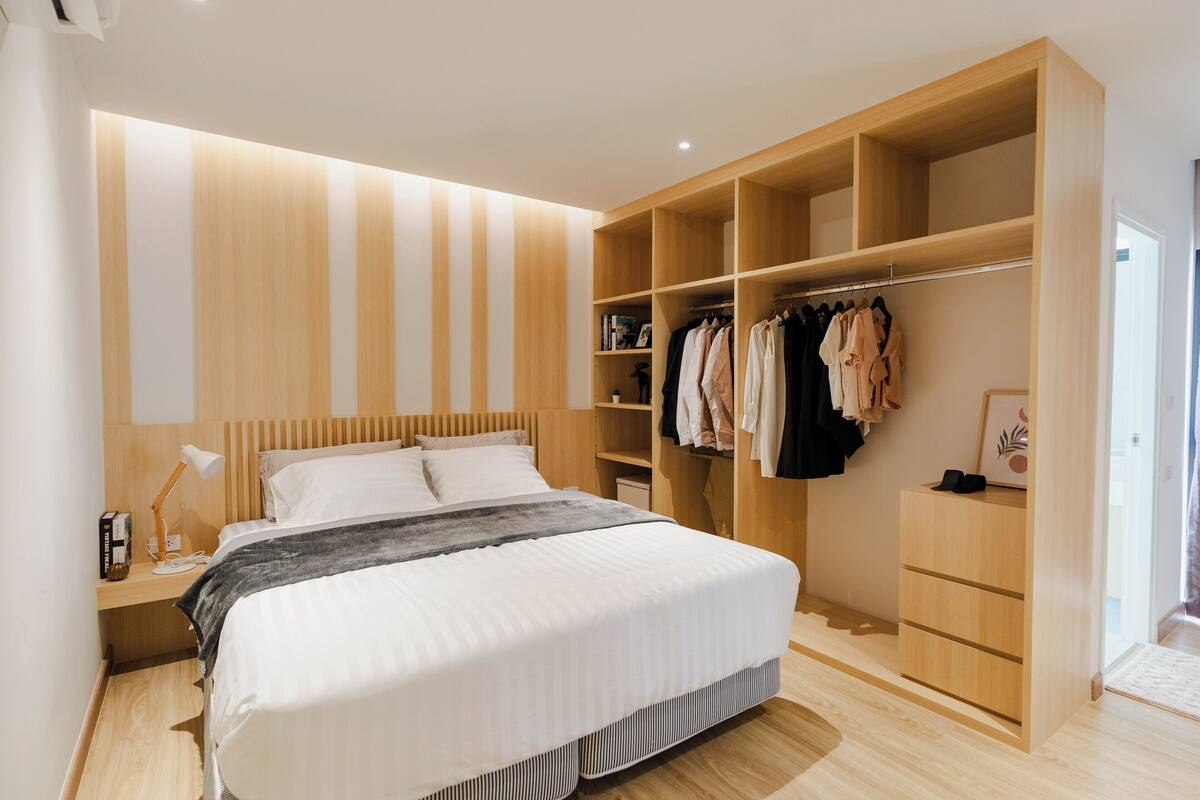 A modern bedroom with a large bed, wooden headboard, built-in wardrobe, and bedside table with lamp.