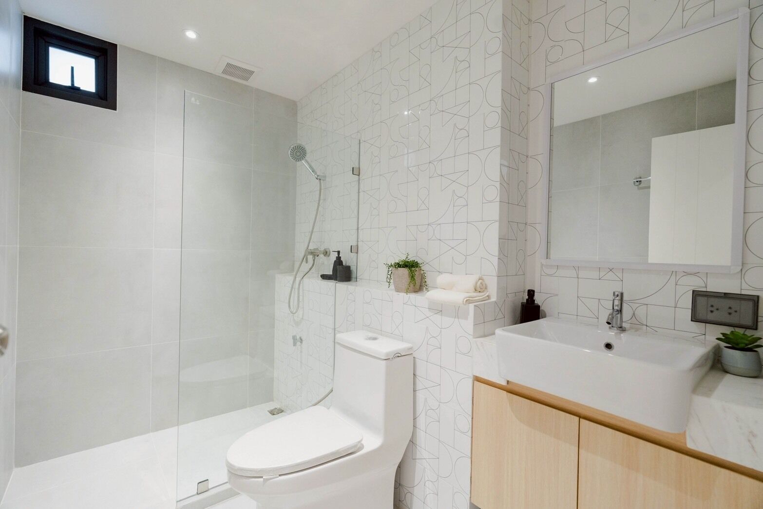 A modern bathroom with a glass-enclosed shower, a toilet, a sink with a mirror, and a wooden cabinet.